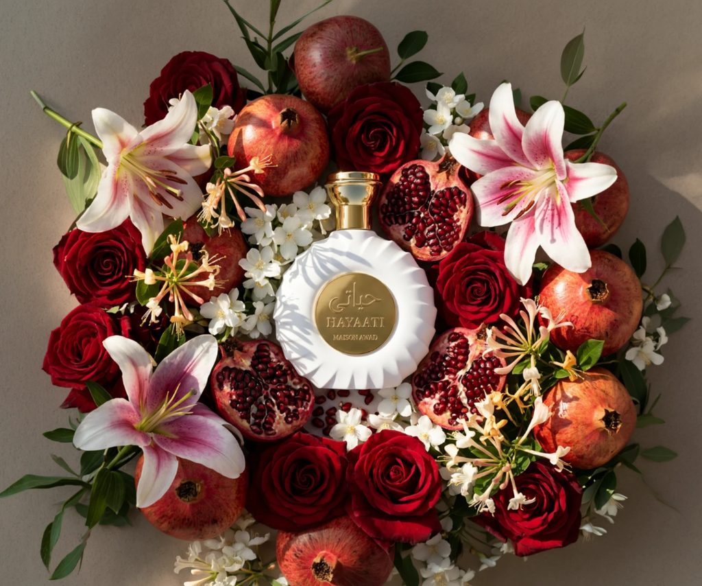 Frasco do perfume Hayaati, da Maison Awad, cercado por rosas, romãs e flores brancas